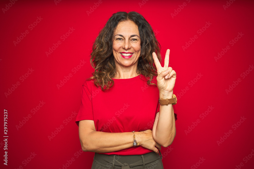 Φωτογραφία Middle age senior woman with curly hair over red isolated background smiling with happy face winking at the camera doing victory sign