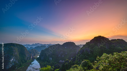 Aerial view at sunset of Ninh Binh region, Tam Coc valley tourist attraction, UNESCO World Heritage Site, scenic river crawling through karst mountain ranges in Vietnam, travel destination.