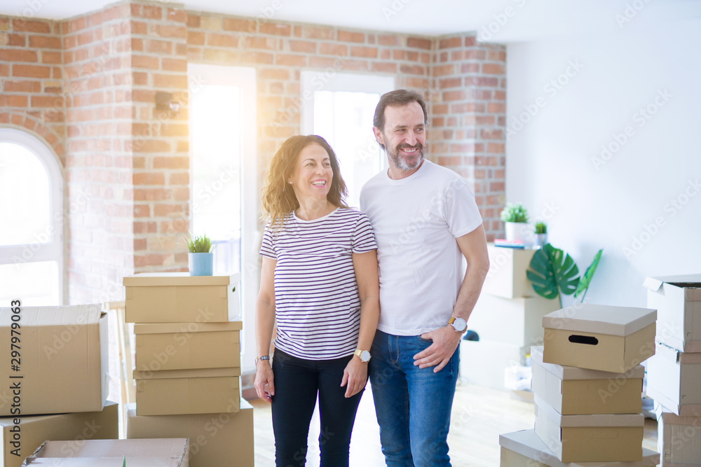 Middle age senior couple moving to a new home with boxes around looking away to side with smile on face, natural expression. Laughing confident. Middle age senior couple moving to a new home with boxes around looking away to side with smile on face, natural expression. Laughing confident.