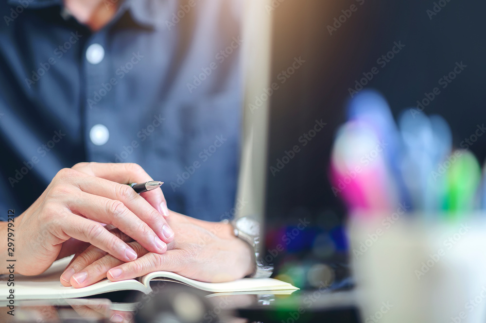 Cropped image of man sitting at office desk holding pen and puting hands together.