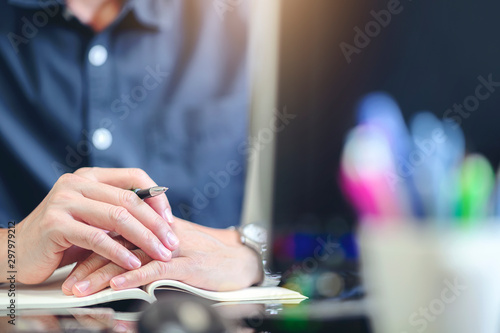 Cropped image of man sitting at office desk holding pen and puting hands together. © NAMPIX