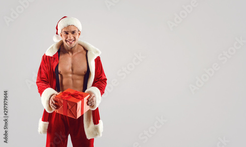 Muscular man in Santa suit holding present