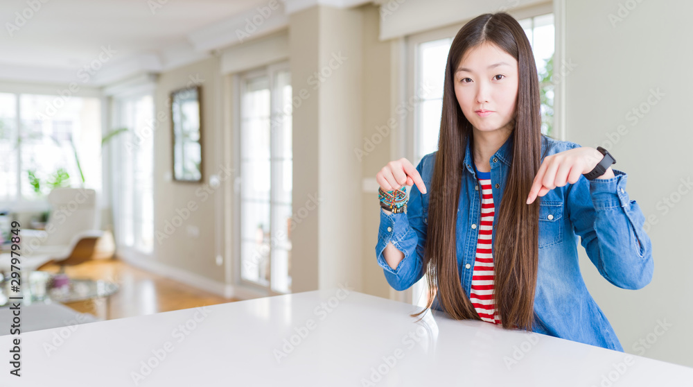 Young beautiful asian woman with long hair wearing denim jacket Pointing down looking sad and upset, indicating direction with fingers, unhappy and depressed. Young beautiful asian woman with long hair wearing denim jacket Pointing down looking sad and upset, indicating direction with fingers, unhappy and depressed.