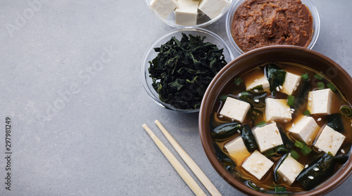 Bowl with miso soup, wakame seaweed, miso pasta, tofu and chopsticks on a gray background. photo
