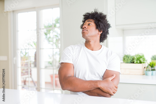 Young african american man wearing casual white t-shirt sitting at home looking to the side with arms crossed convinced and confident