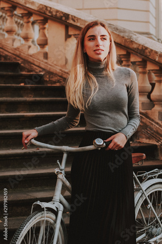 Stylish autumn fashionable image of a girl. Gray blazer and pleats skirt. Blonde woman, white bicycle.