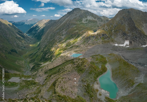 AERIAL; panorama of highland landscape with alpine turquoise lakes, white glacier, dangerous steep rocky slope of mountain ridge Chilipsi; river valley, green high meadows; natural tourism background