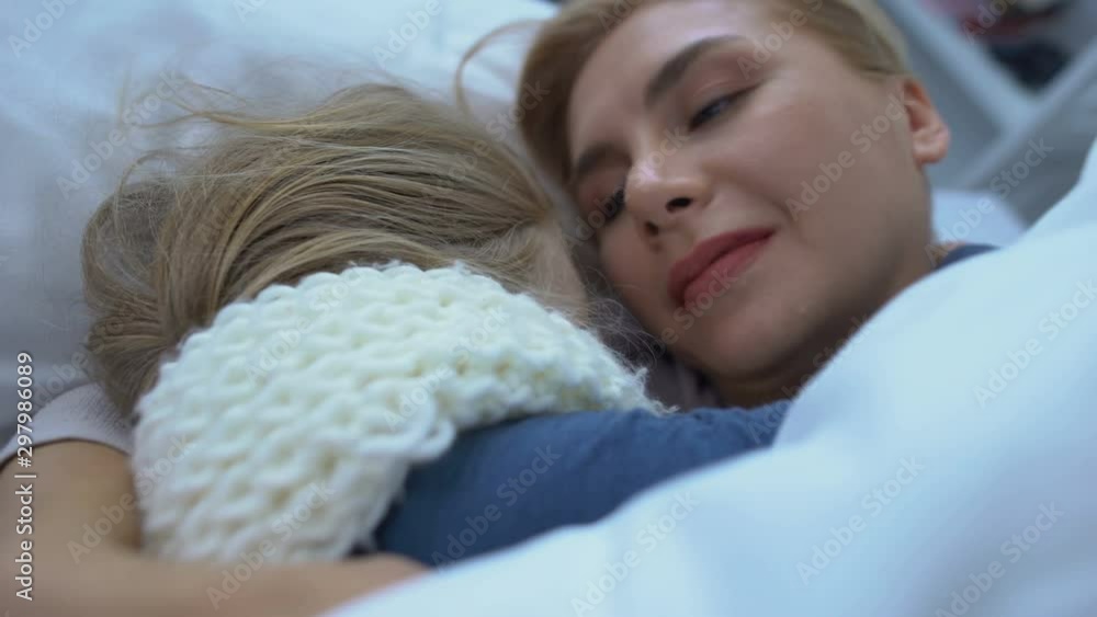 Little sick girl in scarf hugging caring mother in bed seasonal disease, support Little sick girl in scarf hugging caring mother in bed seasonal disease, support