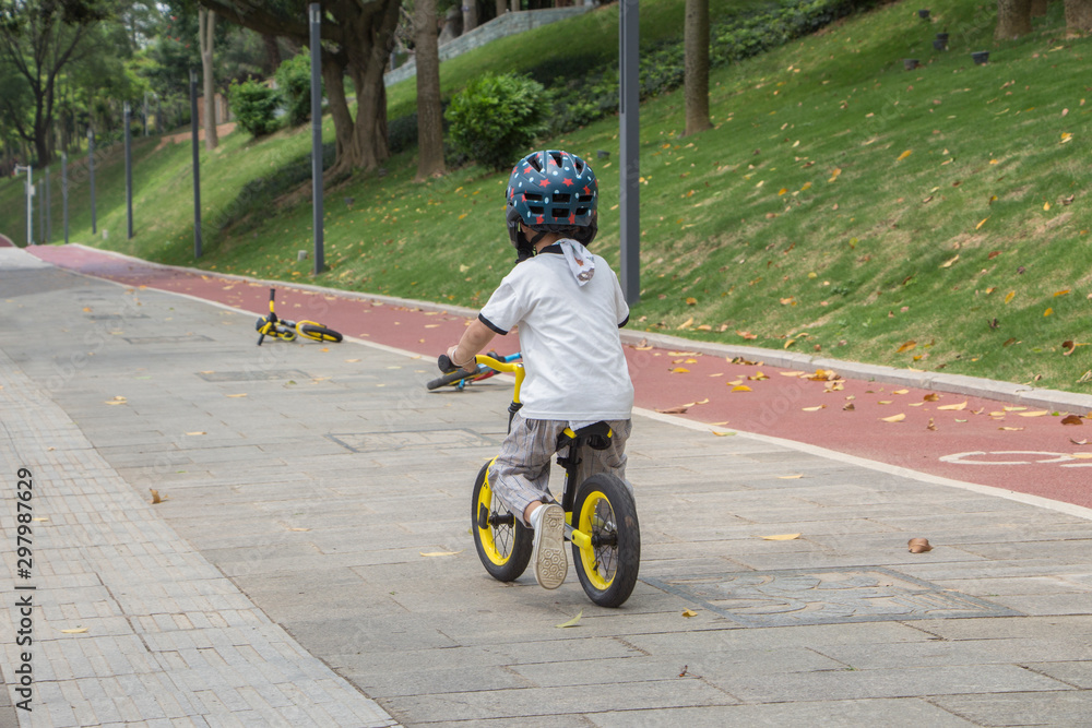 Obraz premium Rear view of a boy wearing a helmet riding a balance bike on a park slate trail