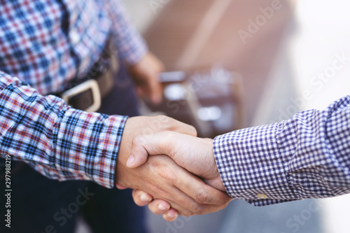 Closeup of a business man with luggage travel hand shake between two colleagues greet, Represents Friendship is good,success, congratulations. outdoor of building background. copy leave space for text