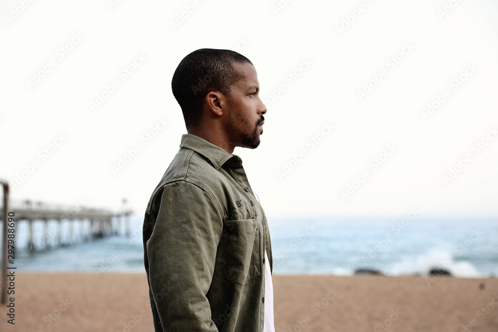 Young black man spending free time on the beach. Wearing casual clothing. Young black man spending free time on the beach. Wearing casual clothing.