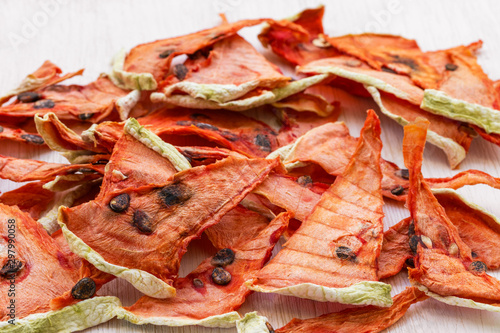Dried watermelon chips lie in a heap on a white wooden background, side view from above
