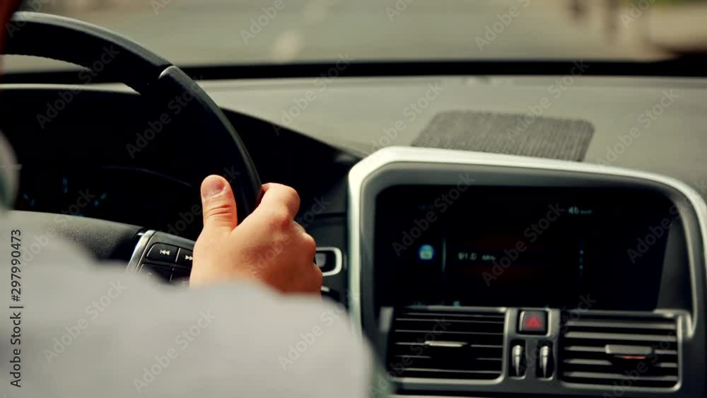 Over the shoulder shot of a handsome man driving his car through the city. Hands Over the shoulder shot of a handsome man driving his car through the city. Hands