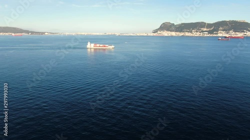 Feeder container vessel passing through Gibraltar Bay.  Some another vessels at anchor. Blue water of the bay.