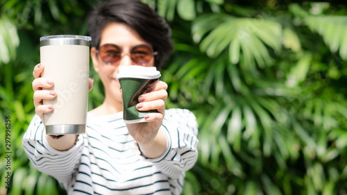 Foto A stylish beautiful woman holding takeaway coffee cup in both hands, one is a single use paper cup with plastic lid the other one is a reusable stainless tumbler