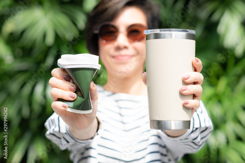 A stylish beautiful woman holding takeaway coffee cup in both hands, one is a single use paper cup with plastic lid the other one is a reusable stainless tumbler. No straw and Zero waste concept. photo