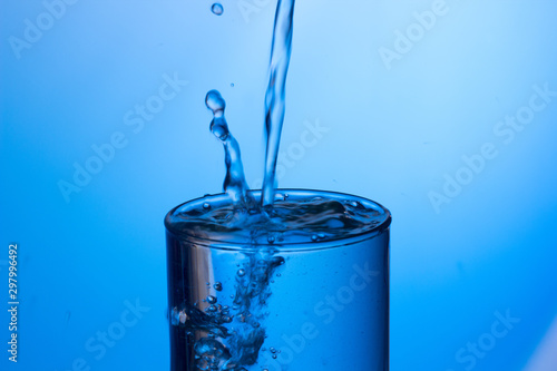 Chorro de agua cayendo sobre un vaso lleno de agua, saltando gotas y chapoteo