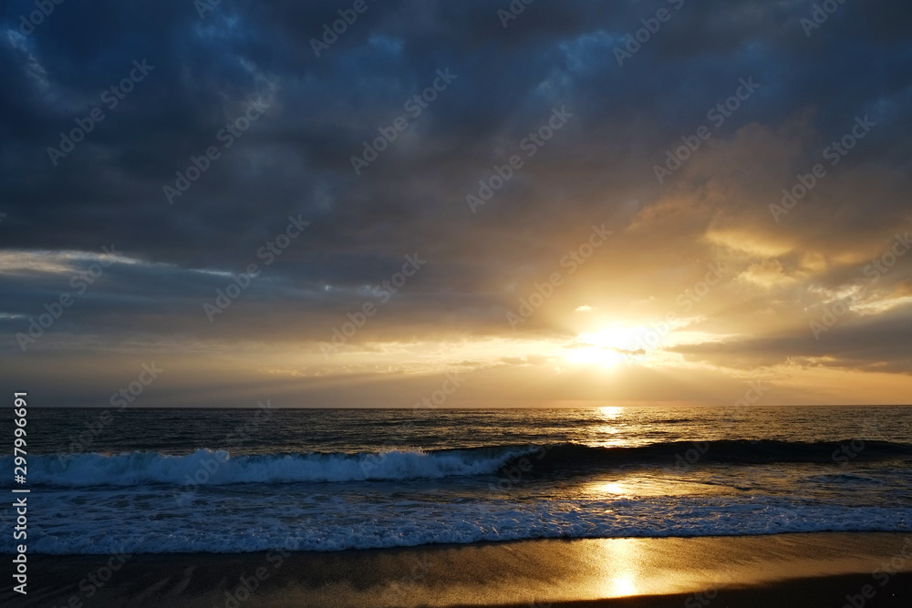 Beautiful seascape of sun setting over calm water with wind patterns and clear blue orange gradient sky without clouds. Ocean view with horizon, background with a lot of copy space for text.