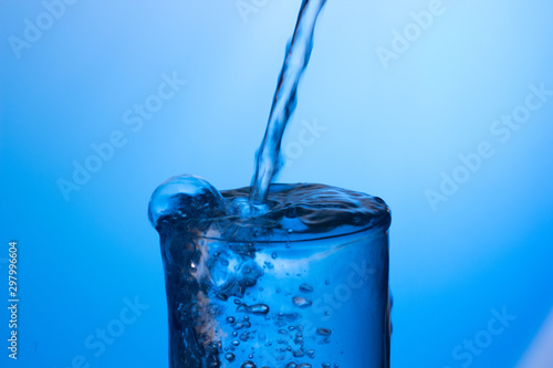 Chorro de agua cayendo sobre un vaso lleno de agua, saltando gotas y chapoteo
