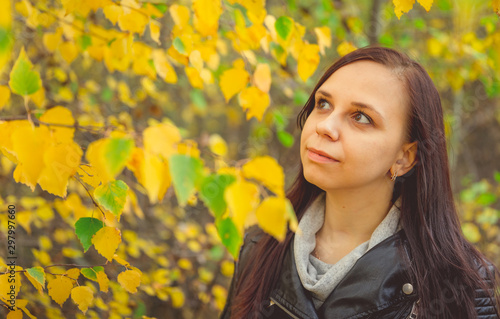 Portrait of a beautiful smiling woman is standing in the autumn forest between the branches of trees with yellow foliage.