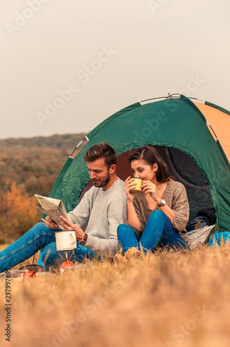 Happy young couple sitting by tent at campsite spending time together in nature looking at map for direction.