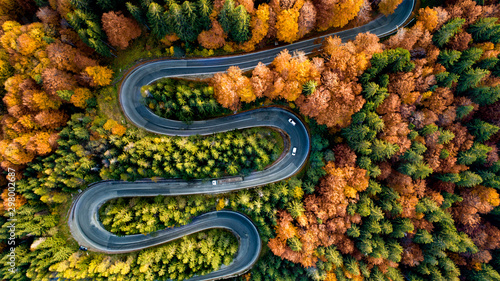 Perfect aerial view of winding forest road in the mountains. Colourful landscape with rural road, trees with yellow leaves.