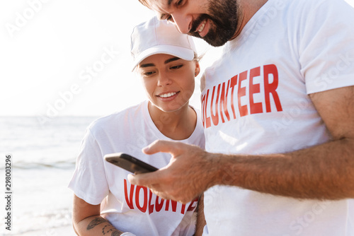 Image of smiling young couple using cellphone while cleaning beach