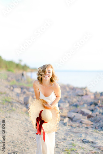 Pretty young woman walking on rocky beach with hant in hands and wearing dress. photo