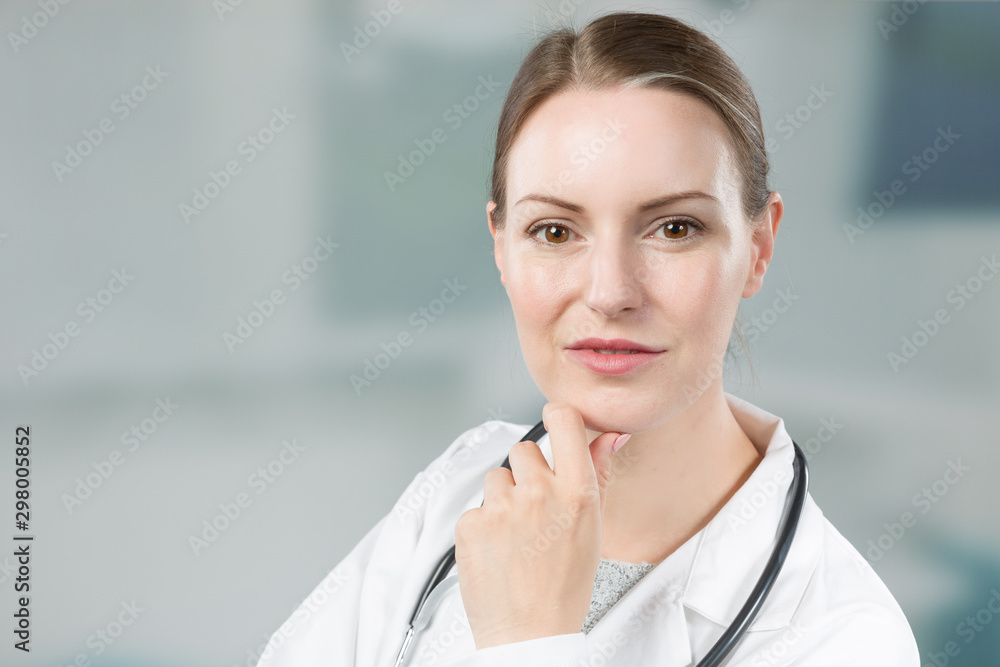 portrait of thinking female family doctor in doctor's overall with stethoscope in front of a clinic room