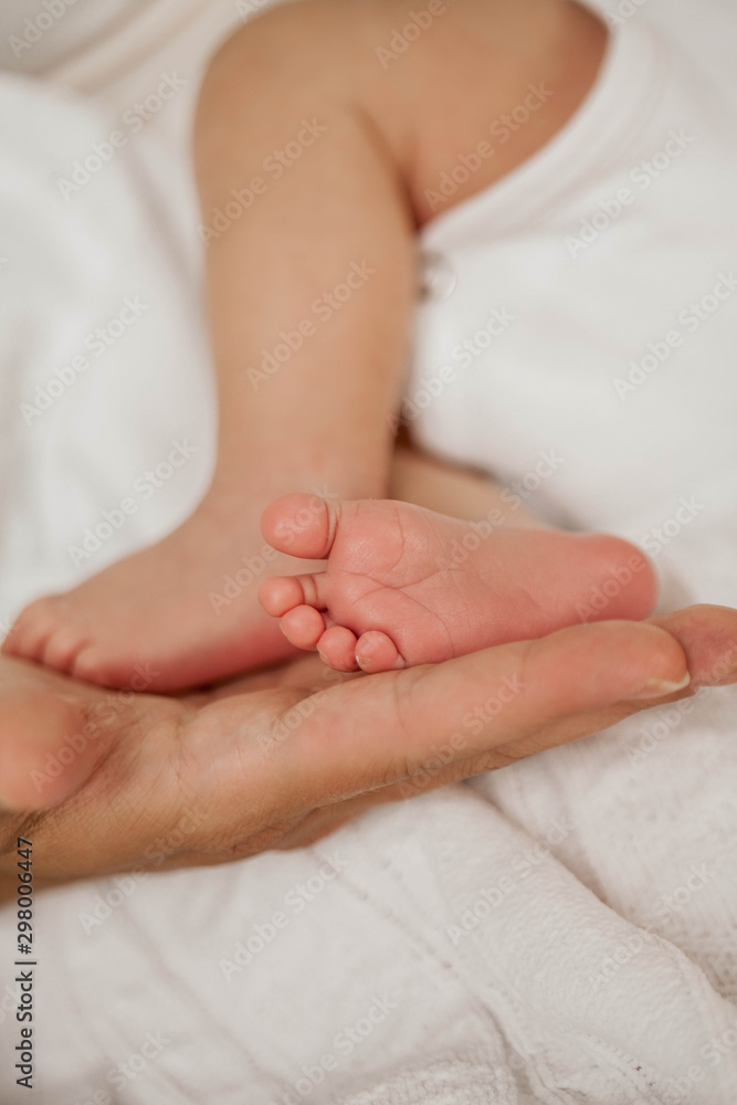 Close-up. Beautiful young mother holds in her hands the legs of the baby. Beautiful young mother plays with the baby in bed. Motherhood. Close-up. Beautiful young mother holds in her hands the legs of the baby. Beautiful young mother plays with the baby in bed. Motherhood.