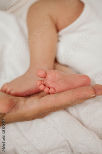 Close-up. Beautiful young mother holds in her hands the legs of the baby. Beautiful young mother plays with the baby in bed. Motherhood.