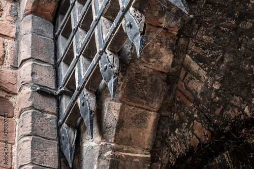 Medieval portcullis gate seen in the opened position at the entrance to a historic building. The sharp, leaded gate and archway can be seen in detail. photo