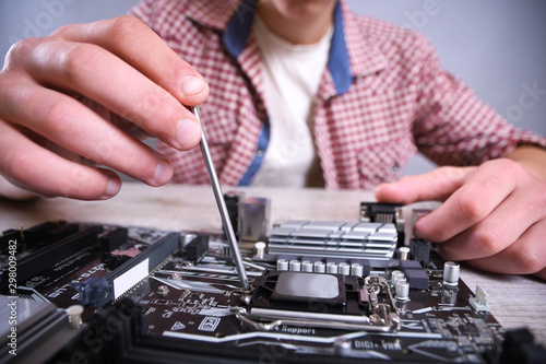 Man repairing broken computer, video card,memory RAM, cooler, processor,hard drive. Young repairer working with screwdriver in service center.teenager