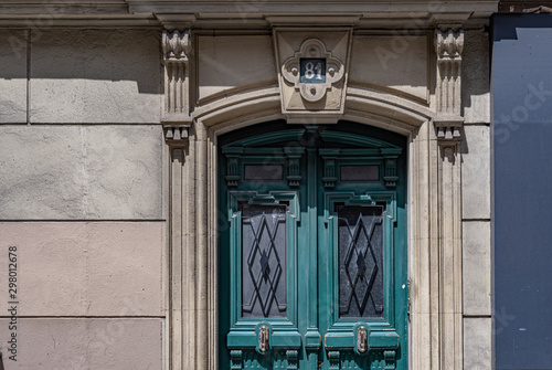 Facade of old house with classical architecture sculptural arch doorway and green painted wooden door with rhombus pattern grids on door windows. Details of Paris door of stone building in France.