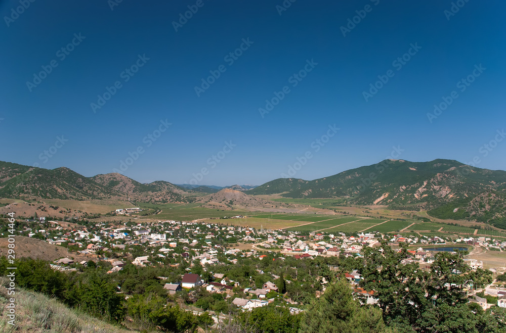 A city in a valley between mountains with fields and vineyards under a blue sky