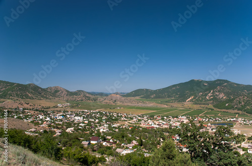 A city in a valley between mountains with fields and vineyards under a blue sky