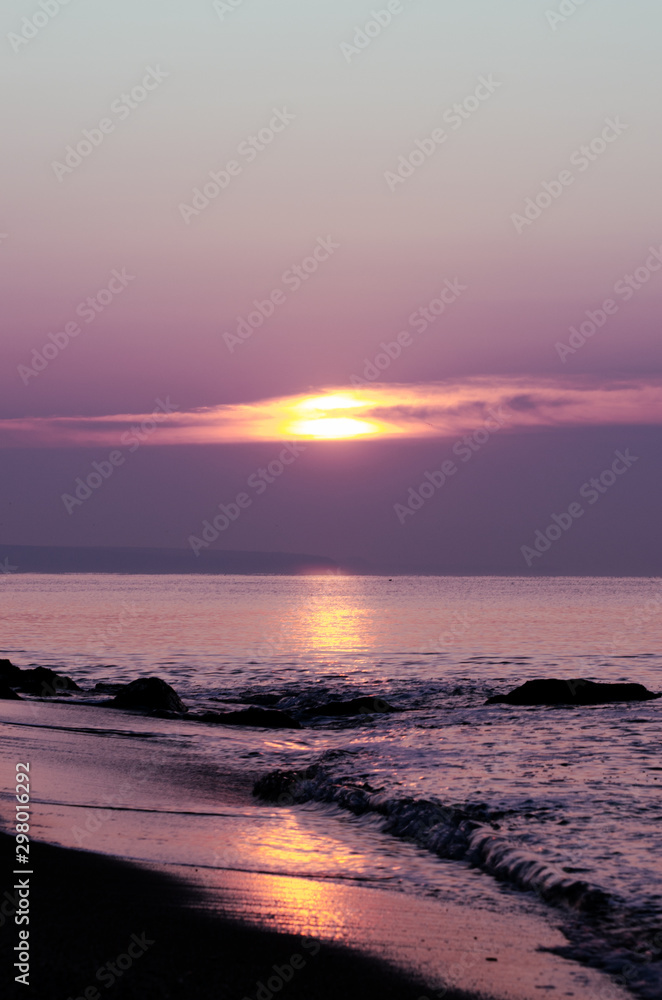 Bright beautiful sunrise at the sea coast. Early morning sun above calm sea surface.