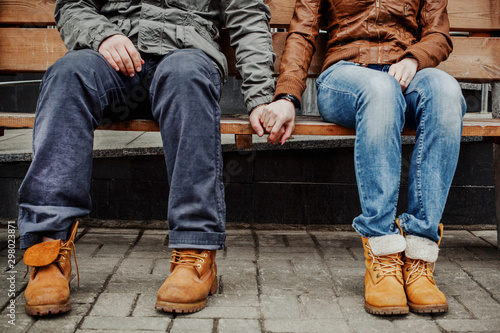 Loving hipster couple in jeans and rough boots sitting on a bench and holding hands © Irina Polonina