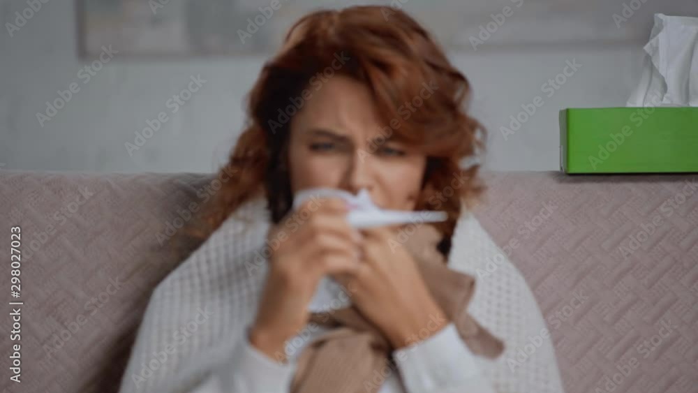 rack focus of sick woman looking at thermometer and sneezing