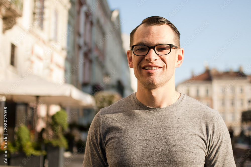 Half body shot of young man in a street of an old town in Europe looking in the camera with brown eyes and eyesglasses Half body shot of young man in a street of an old town in Europe looking in the camera with brown eyes and eyesglasses