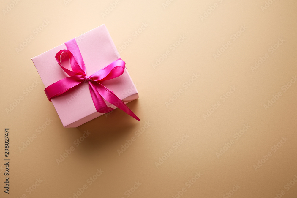 top view of pink gift box with ribbon on beige background