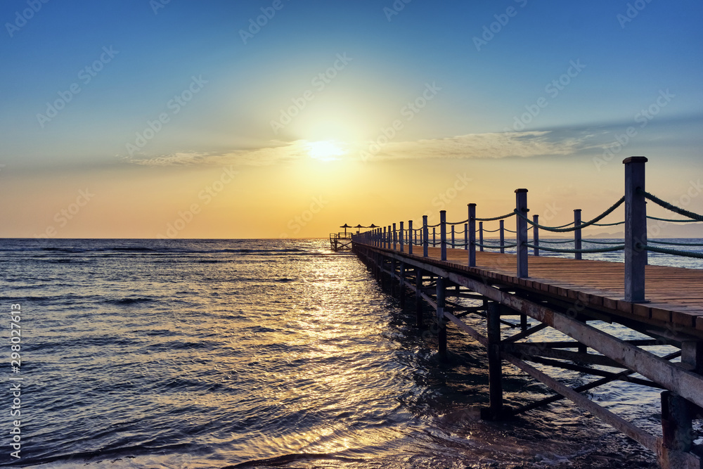Bright and colorful sunrise over the pier and sea. Perspective view of a wooden pier on the sea at sunrise with rocky islands in the distance