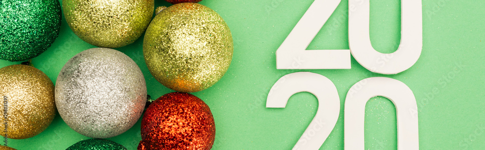 top view of white 2020 numbers near multicolored Christmas baubles on green background, panoramic shot top view of white 2020 numbers near multicolored Christmas baubles on green background, panoramic shot