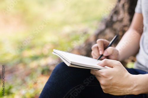 Bilde på lerret close up hand young man are sitting using pen writing Record Lecture notepad into the book in the park