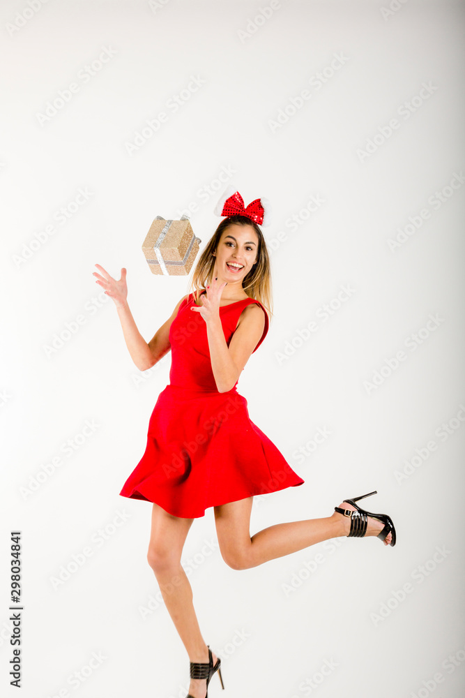 Obraz premium Happy excited young woman in santa claus hat with gift box over gray background