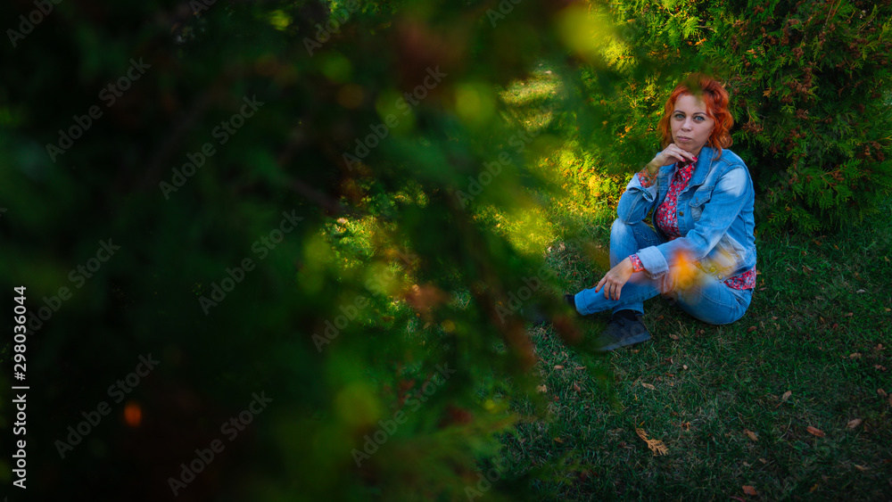 Young woman with red hair among trees. Portrait of young attractive female with trendy hairstyle standing in spring garden and looking at camera Young woman with red hair among trees. Portrait of young attractive female with trendy hairstyle standing in spring garden and looking at camera