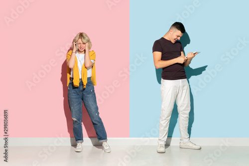 Young emotional man and woman in bright casual clothes posing on pink and blue background. Concept of human emotions, facial expession, relations, ad. Woman's sad, man's astonished, crazy happy.