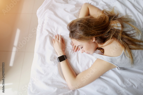 portrait of young woman sleeping with smart watches on hand in white bed