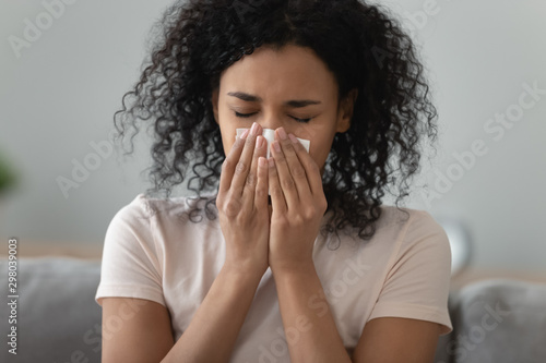 Ill black young woman having rhinitis blowing nose