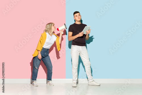 Young emotional man and woman in bright casual clothes posing on pink and blue background. Concept of human emotions, facial expession, relations, ad. Man's ignoring woman with mouthpeace.